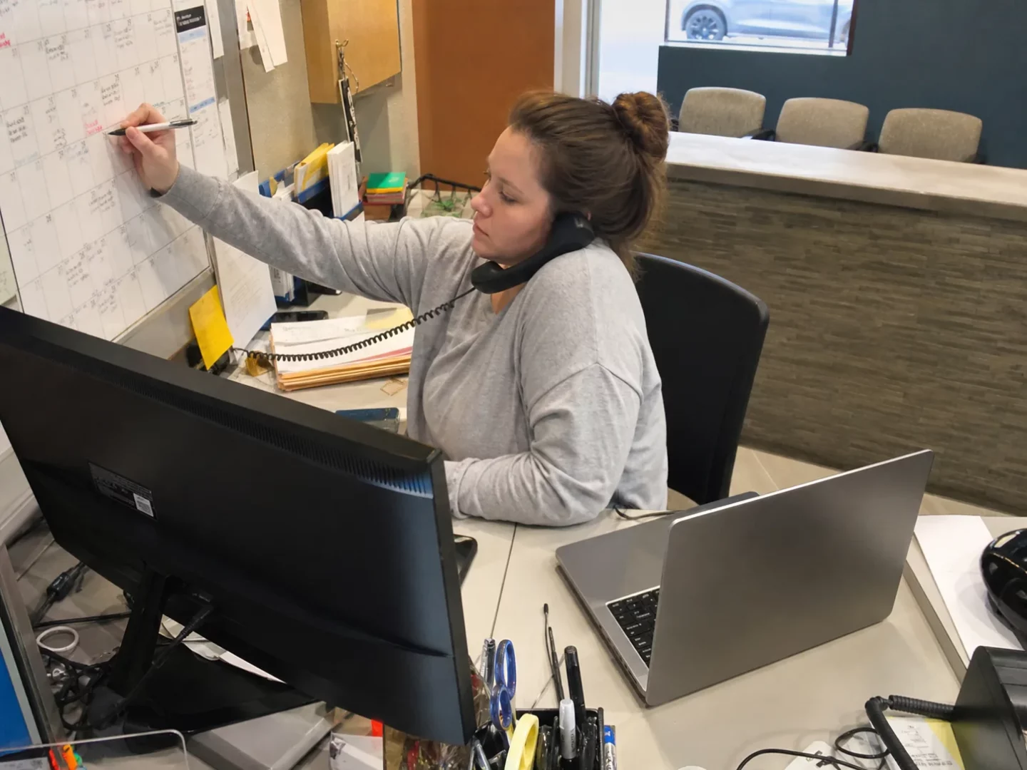 Receptionist checking a calendar and laptop during an appointment call