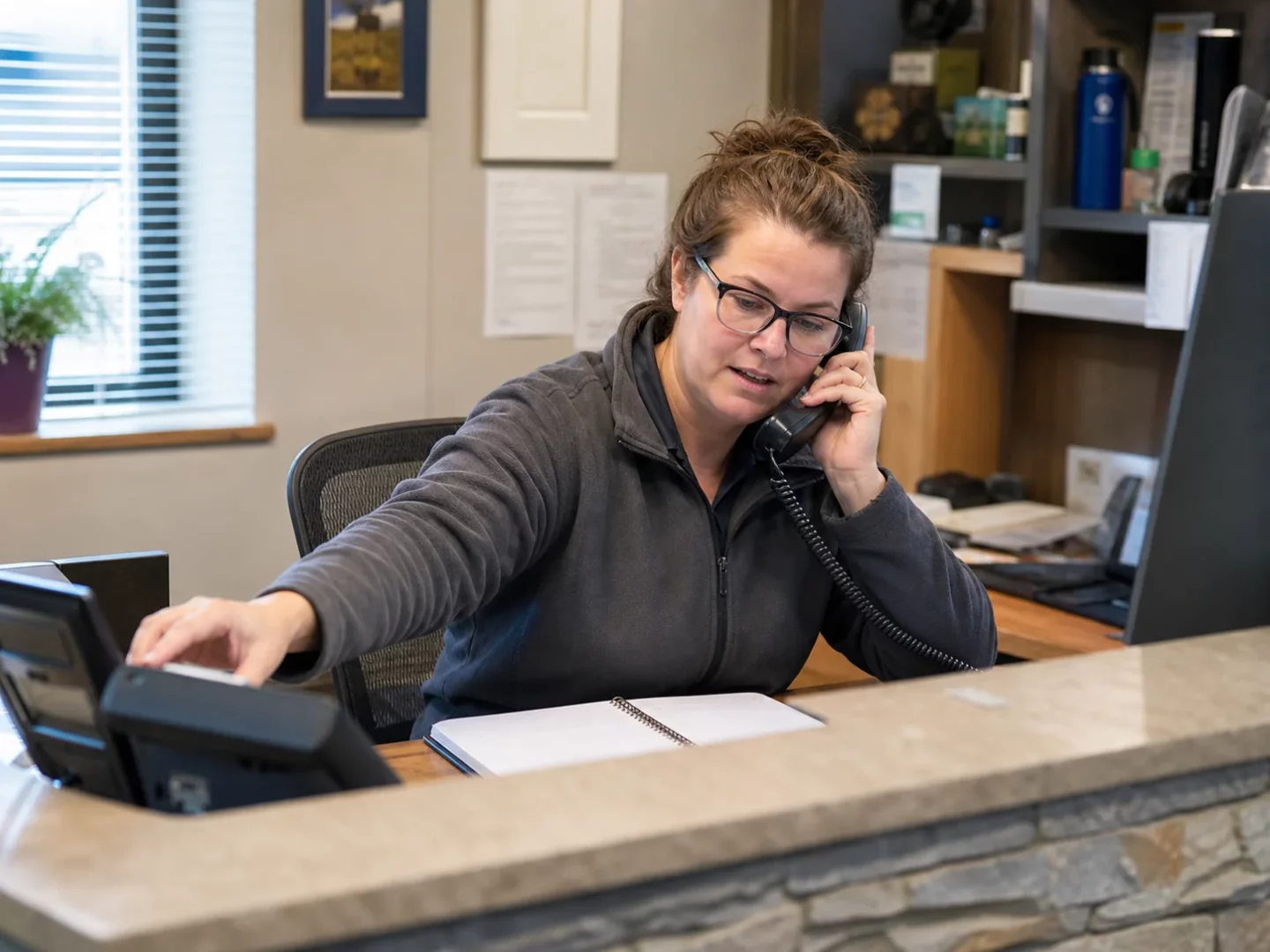Receptionist handling a call beside an on call phone and dispatcher notebook