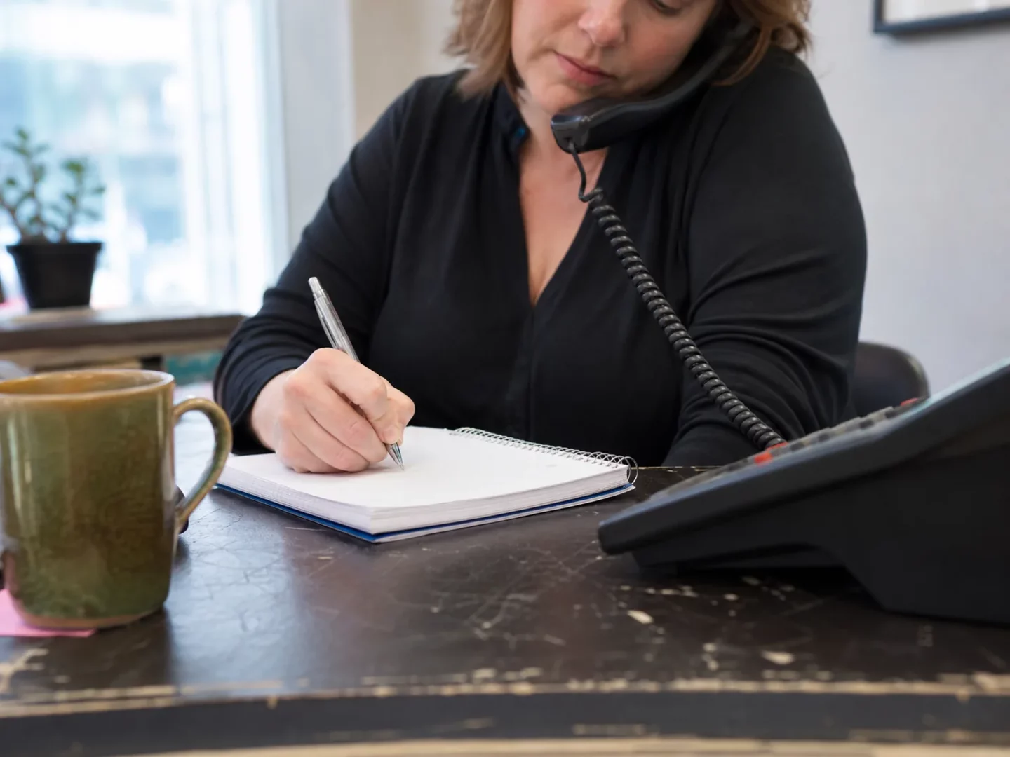 Receptionist recording essential caller information beside a phone